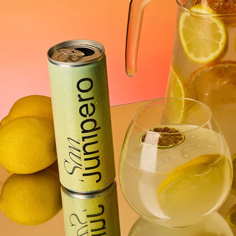 Can of San Junipero Limoncello with a glass of San Junipero and lemons on an orange background